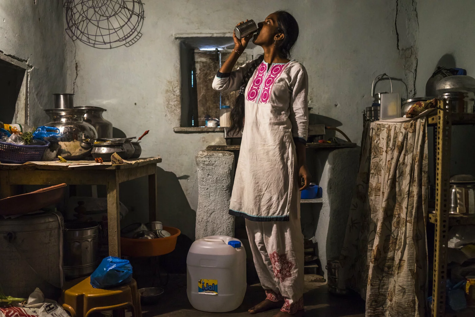 Cheekata  Srujana, 18, drinks a cup of water as she waits for a meal to cook in her kitchen in Peddapur, a remote village in Warangal, Telangana, India, on 22nd March 2015. Cheekata only uses safe water for all her cooking and drinking needs of the family. Photo by Suzanne Lee/Panos Pictures for Safe Water Network 2023/08/Photo-3.jpg 